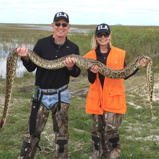 A couple holding a Burmese python stretched out amongst them